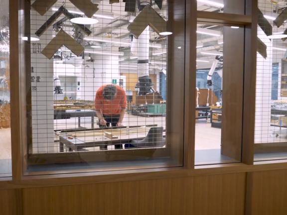 An MFA conservator treating elements of a frame as seen through the glass windows of the Conservation Center