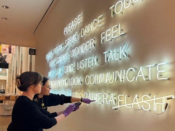 Conservators standing in front of a large neon display installed on a wall examining and discussing its condition