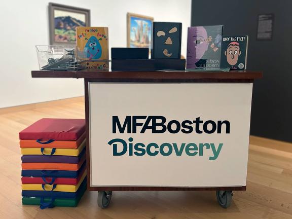 Discovery Cart in gallery with books and clipboards arranged on surface and pile of multi-colored mats adjacent